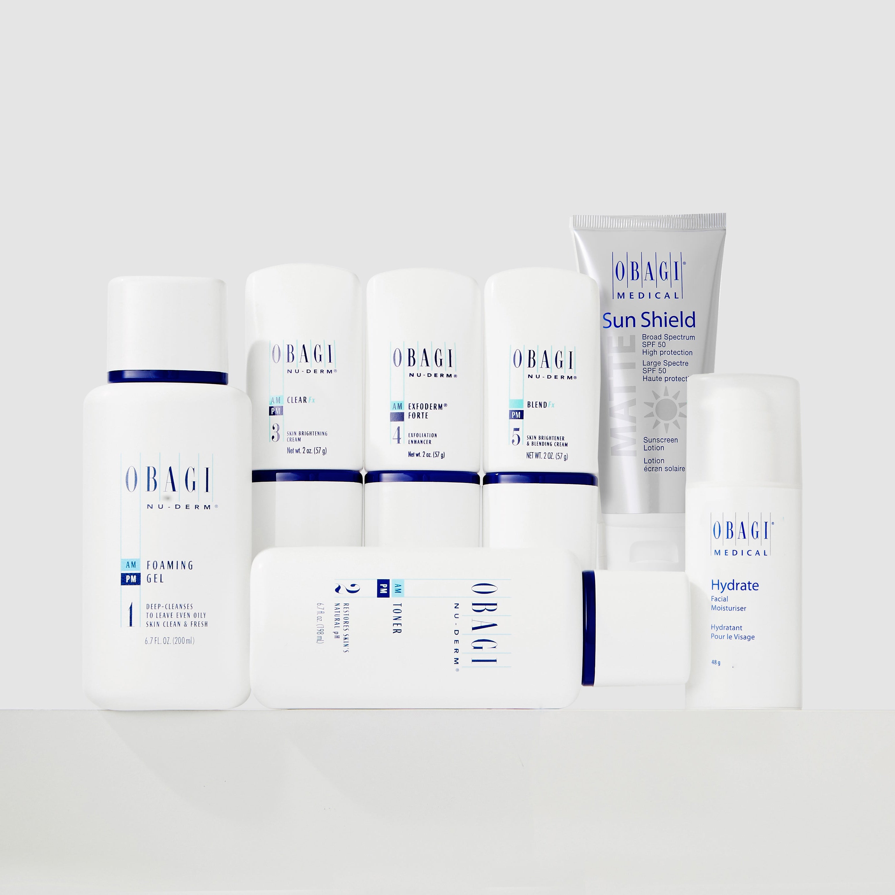 A group of OBAGI MEDICAL skincare products arranged on a white surface against a light gray background. The products include a Control Gel bottle, several white tubes and bottles, a Hyaluader bottle, and a Sun Shield tube.